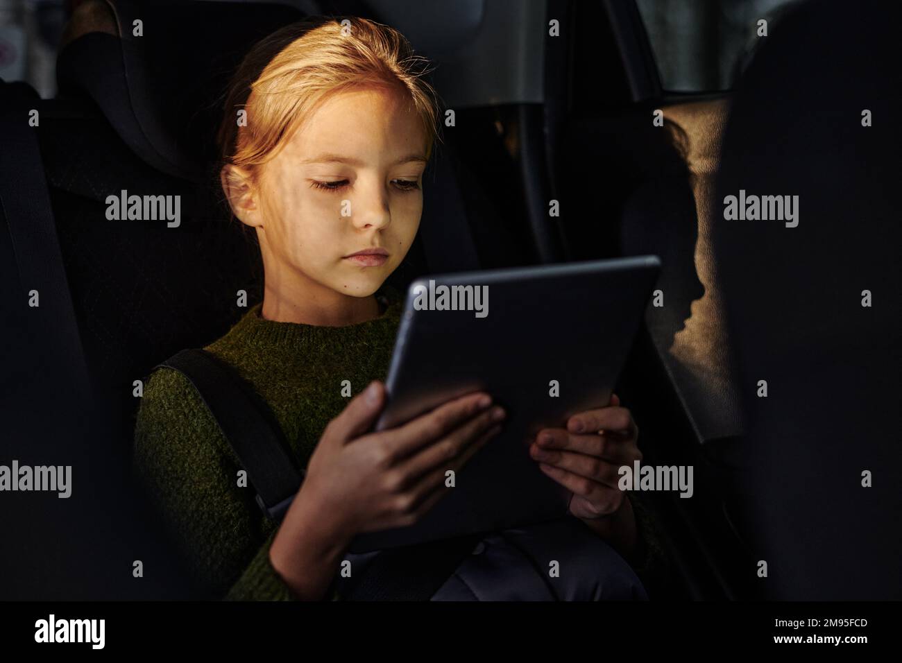 Petite fille regardant des dessins animés sur une tablette numérique tout en étant assise sur la banquette arrière pendant le voyage en voiture Banque D'Images
