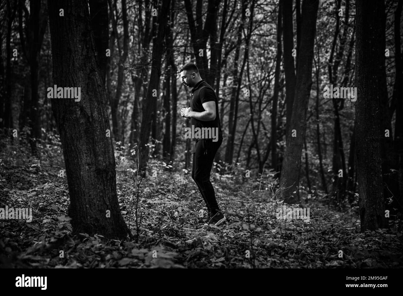 Photo en niveaux de gris d'un beau homme debout dans une forêt Banque D'Images