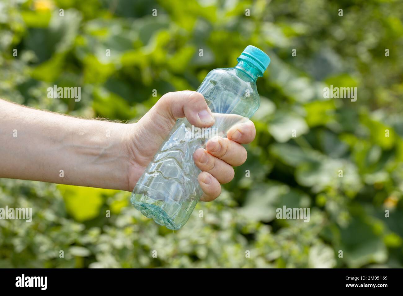 Main tenant une bouteille en plastique vide froissés dans le parc Banque D'Images