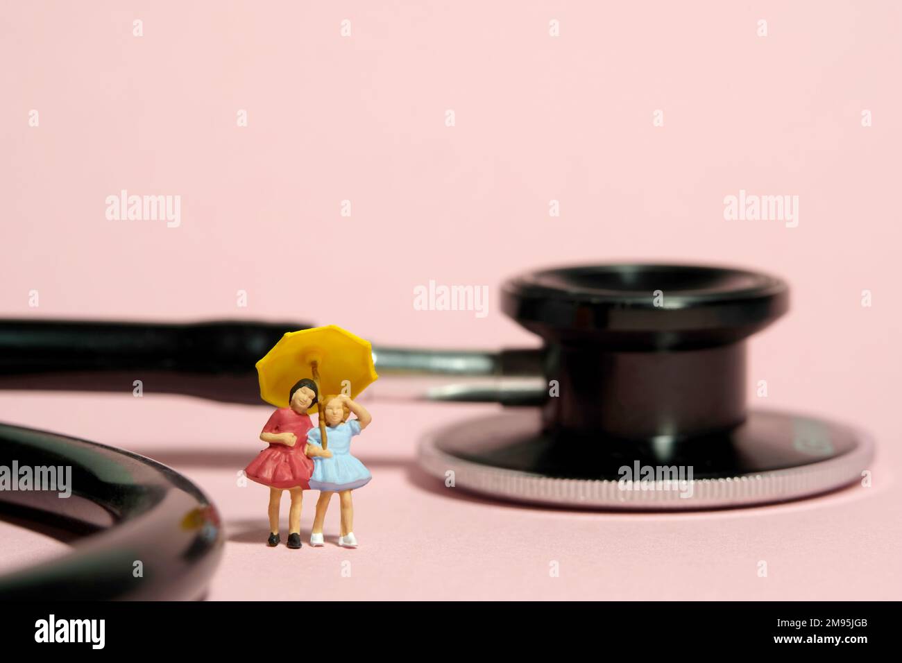 Photographie miniature de personnage de jouet de personnes. Deux filles enfant debout à côté du stéthoscope à l'aide d'un parapluie. Isolé sur fond rose. Photo d'image Banque D'Images