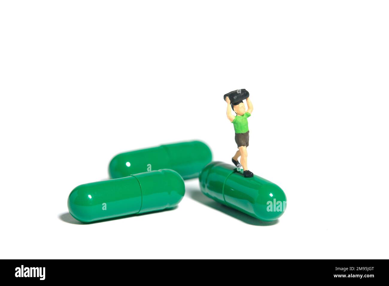 Photographie miniature de personnage de jouet de personnes. Garçon étudiant courant au-dessus de la pilule verte de vitamine pour le traitement de la grippe. Isolé sur fond blanc. Transfert d'image Banque D'Images