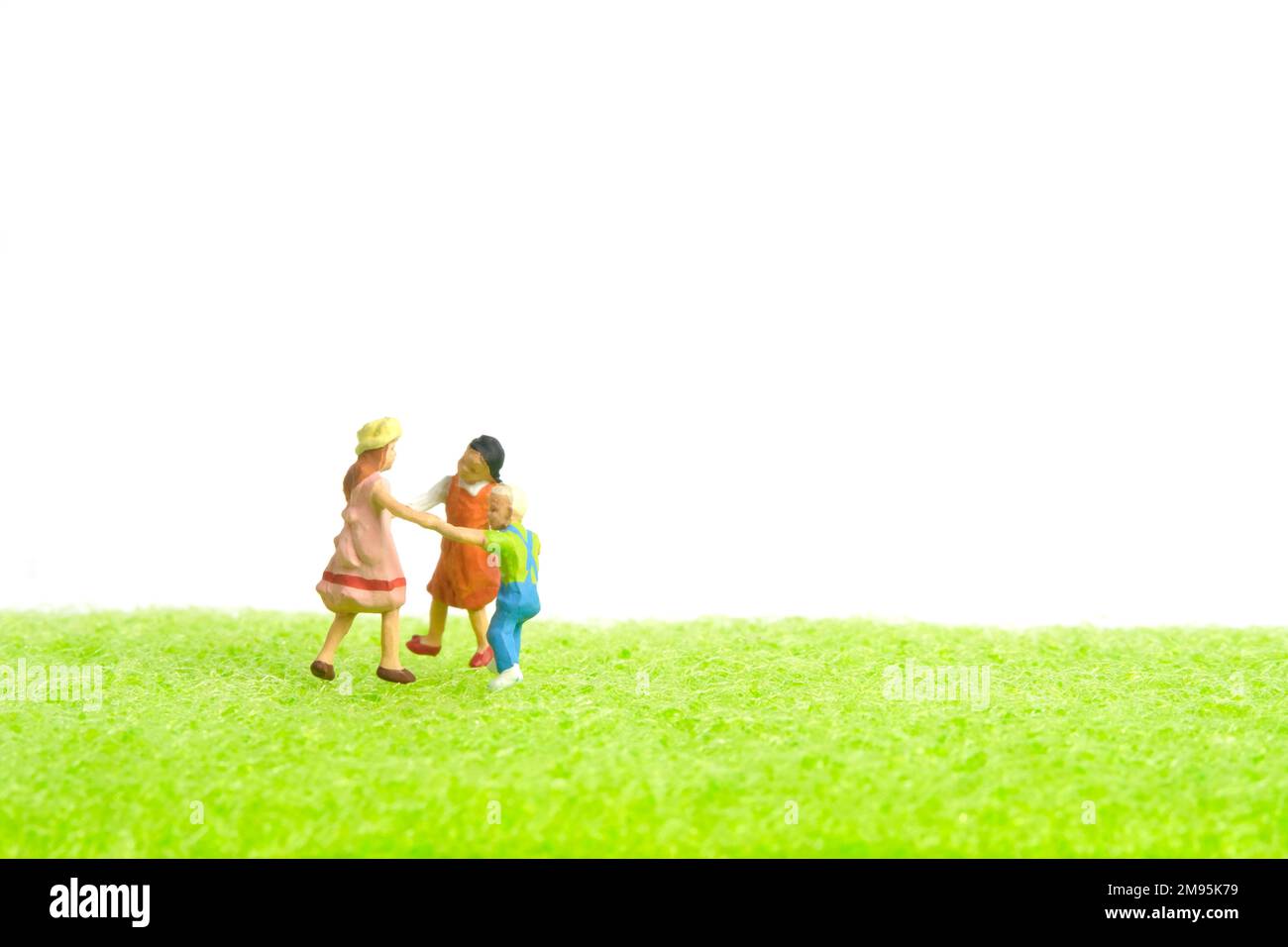 Photographie miniature de personnage de jouet de personnes. Concept d'arène de jeux. Les enfants jouent ensemble au-dessus de l'herbe verte. Isolé sur fond blanc. Image Banque D'Images