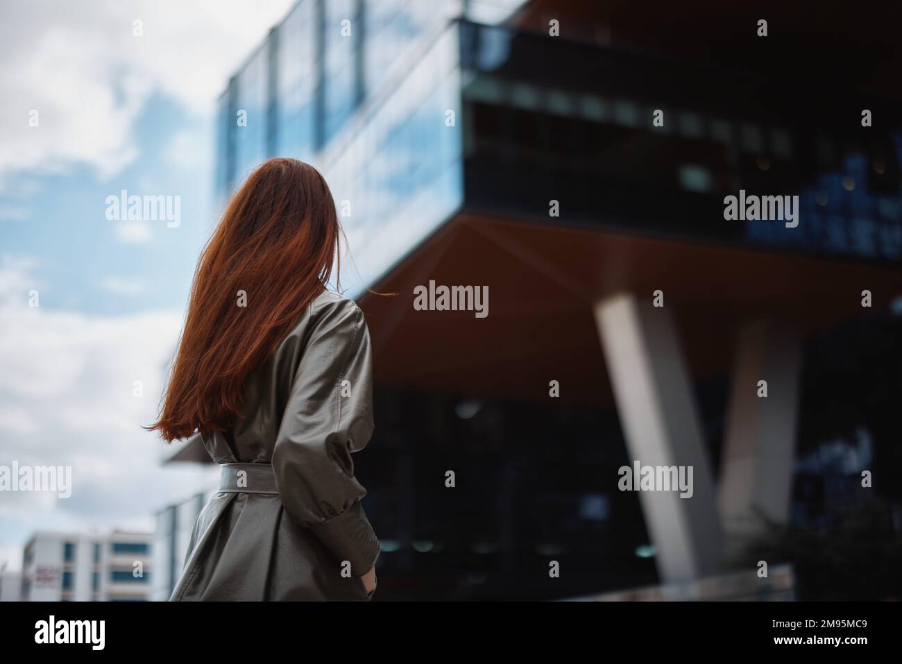 Jeune femme d'affaires parlant au téléphone avec un sourire et des cheveux rouges devant de grands bâtiments dans la ville, le concept de la technologie et des affaires Banque D'Images
