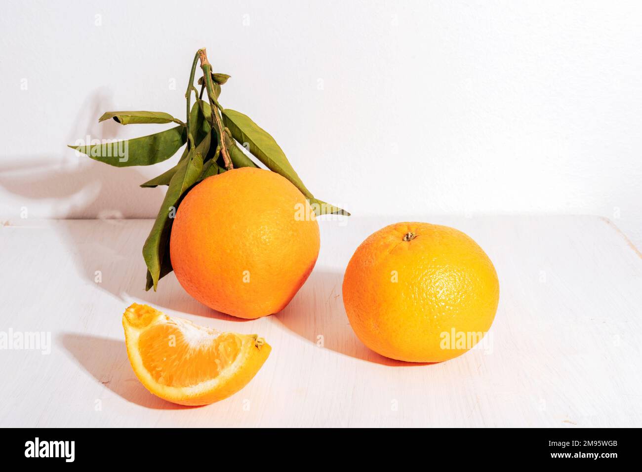 Oranges fraîches mûres avec feuilles et tranche d'orange sur table blanche au soleil. Concept d'alimentation saine, gros plan. Banque D'Images