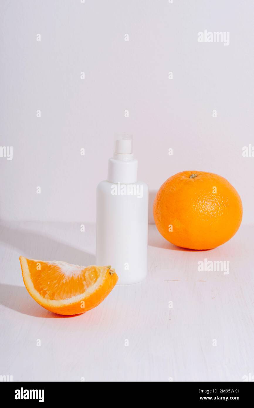 Bouteille de sérum cosmétique et fruit orange sur fond blanc. Concept de cosmétiques naturels, maquette. Banque D'Images