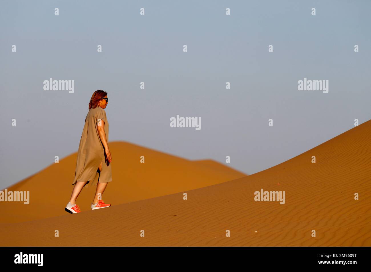 Femme marchant seule sur une dune de sable vers le désert arabe. Émirats arabes Unis. Banque D'Images