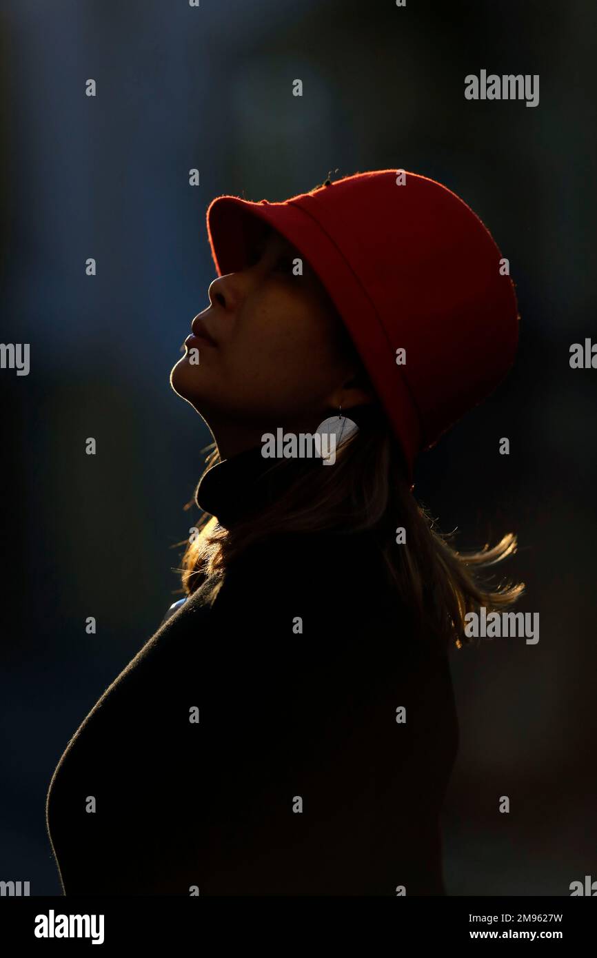 Vue de profil de la femme silhouette portant un rouge debout à l'extérieur pendant le coucher du soleil. Banque D'Images
