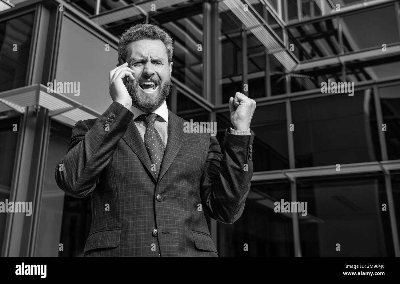 un entrepreneur en colère en costume criant pendant une conversation téléphonique à l'extérieur du bureau, frustration. Banque D'Images