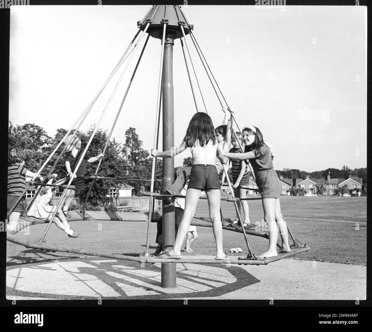 Enfants jouant sur un rond-point "parapluie" sur Lindfield Common, Sussex, Angleterre. Banque D'Images