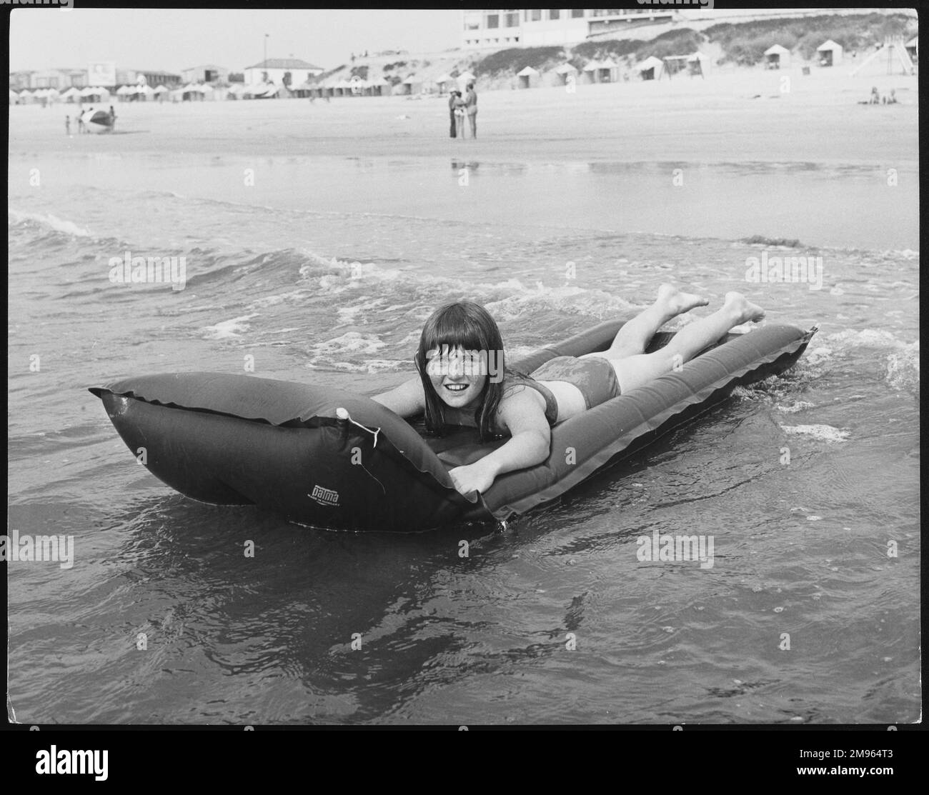 Une fille heureuse sur un lilo gonflable dans ce qui ressemble à l'eau de mer plutôt froide! Banque D'Images
