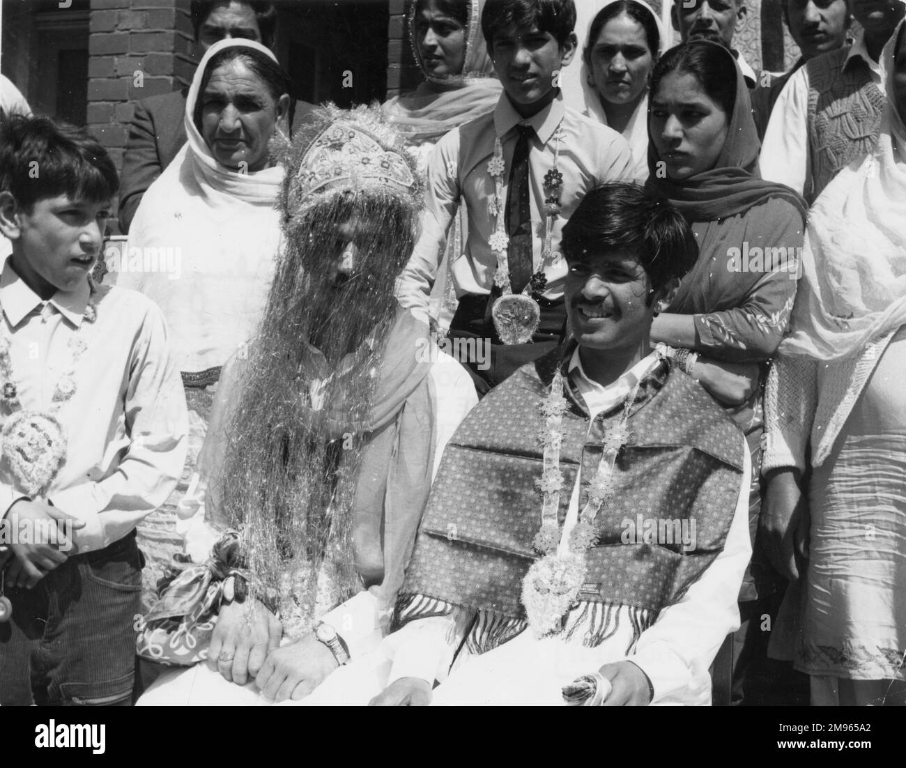 Scène à un mariage musulman (pakistanais), probablement en Grande-Bretagne, avec le marié portant une robe de tête, entouré de sa famille. Banque D'Images