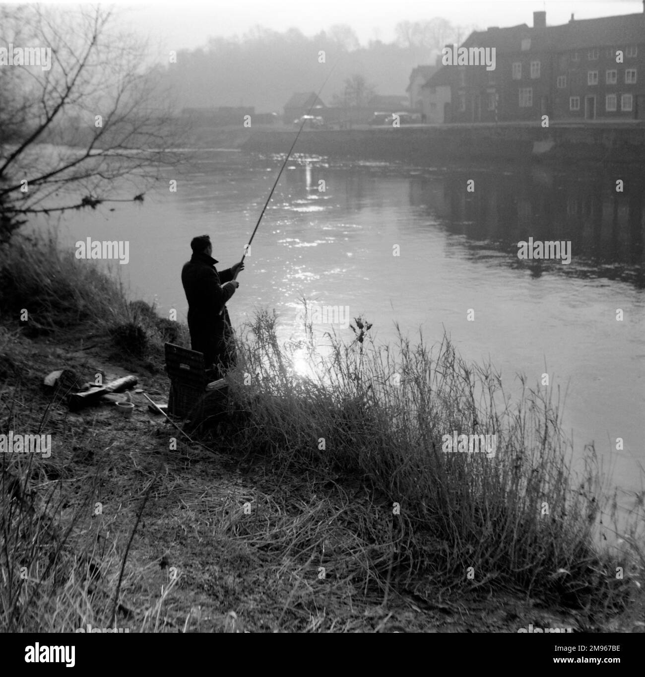 Un pêcheur à la ligne jette sa ligne dans la rivière Severn dans la lumière brumeuse du matin à Bewdley, Worcestershire. Photographie de Norman Synge Waller Budd Banque D'Images