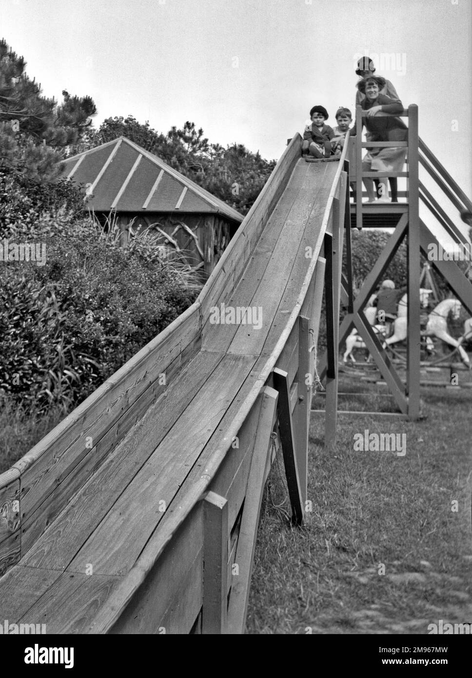 Deux enfants, une fille et un garçon, avec deux femmes au sommet d'une aire de jeux en bois à Bexhill, Sussex. Des chevaux au rond-point peuvent être vus en arrière-plan. Banque D'Images