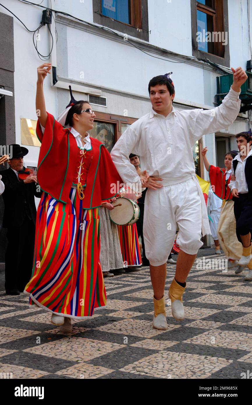 Deux membres d'un groupe folklorique de Gaula, vu ici dansant à Funchal, la capitale de Madère, avec des musiciens jouant en arrière-plan. Le couple porte un costume traditionnel, y compris des têtes de crâne noires avec des points. La femme porte la plupart du temps rouge, y compris une longue jupe à rayures. L'homme est habillé en blanc. Banque D'Images
