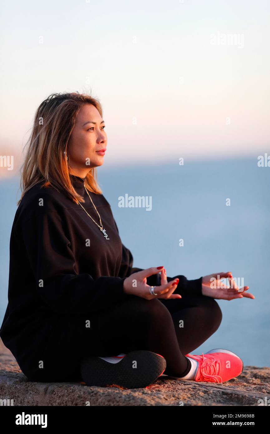 Femme pratiquant la méditation de yoga au bord de la mer avant le coucher du soleil comme concept de silence, d'harmonie et de détente. Banque D'Images