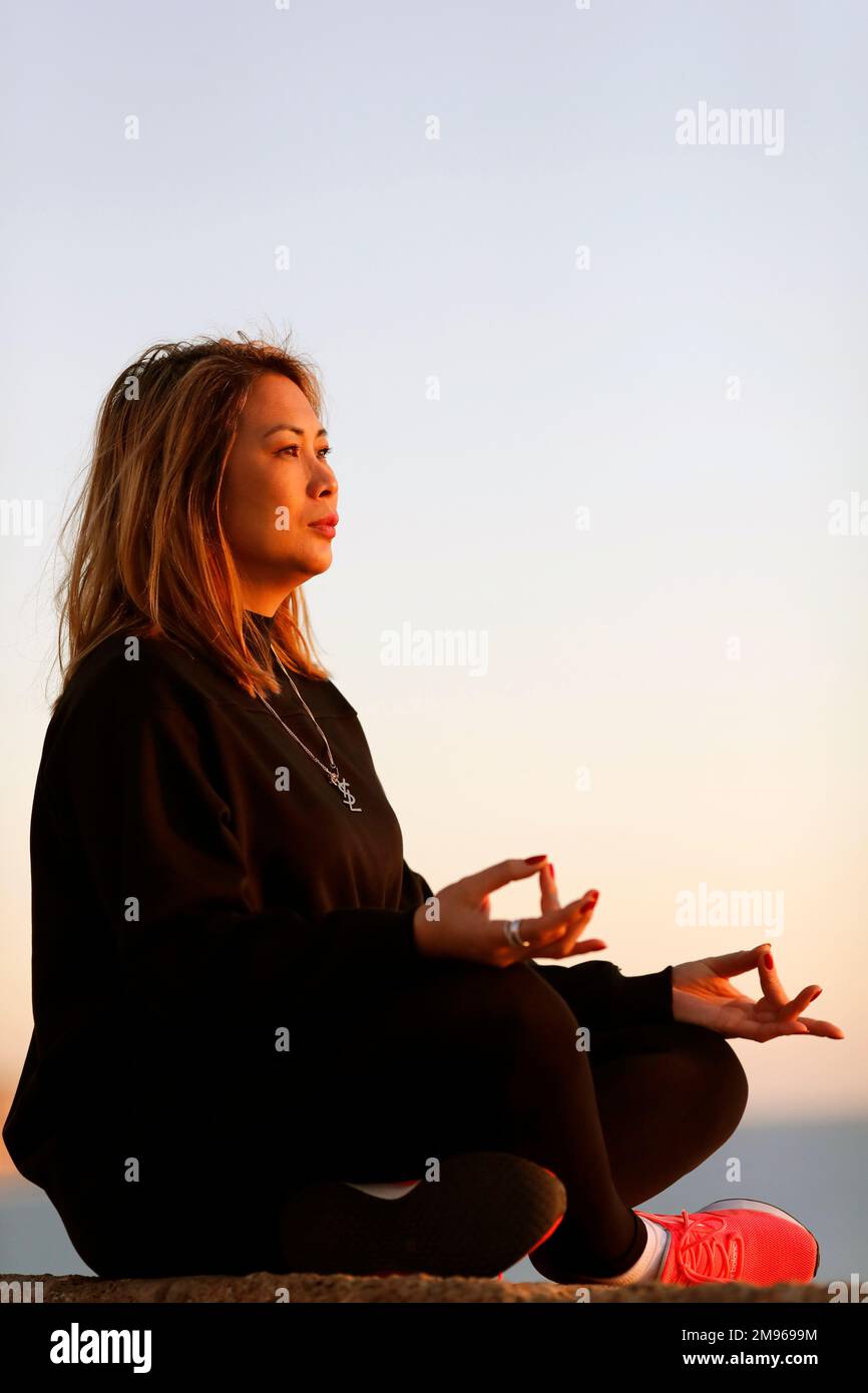 Femme pratiquant la méditation de yoga au bord de la mer avant le coucher du soleil comme concept de silence, d'harmonie et de détente. Banque D'Images