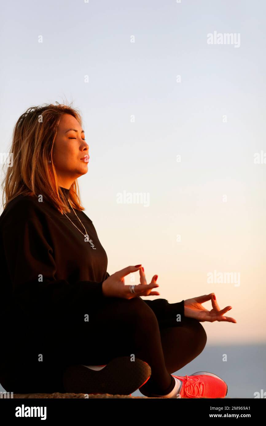 Femme pratiquant la méditation de yoga au bord de la mer avant le coucher du soleil comme concept de silence, d'harmonie et de détente. Banque D'Images