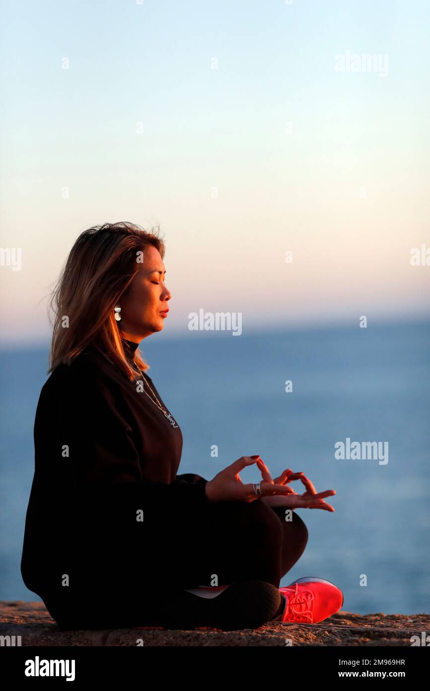 Femme pratiquant la méditation de yoga au bord de la mer avant le coucher du soleil comme concept de silence et de détente. Banque D'Images