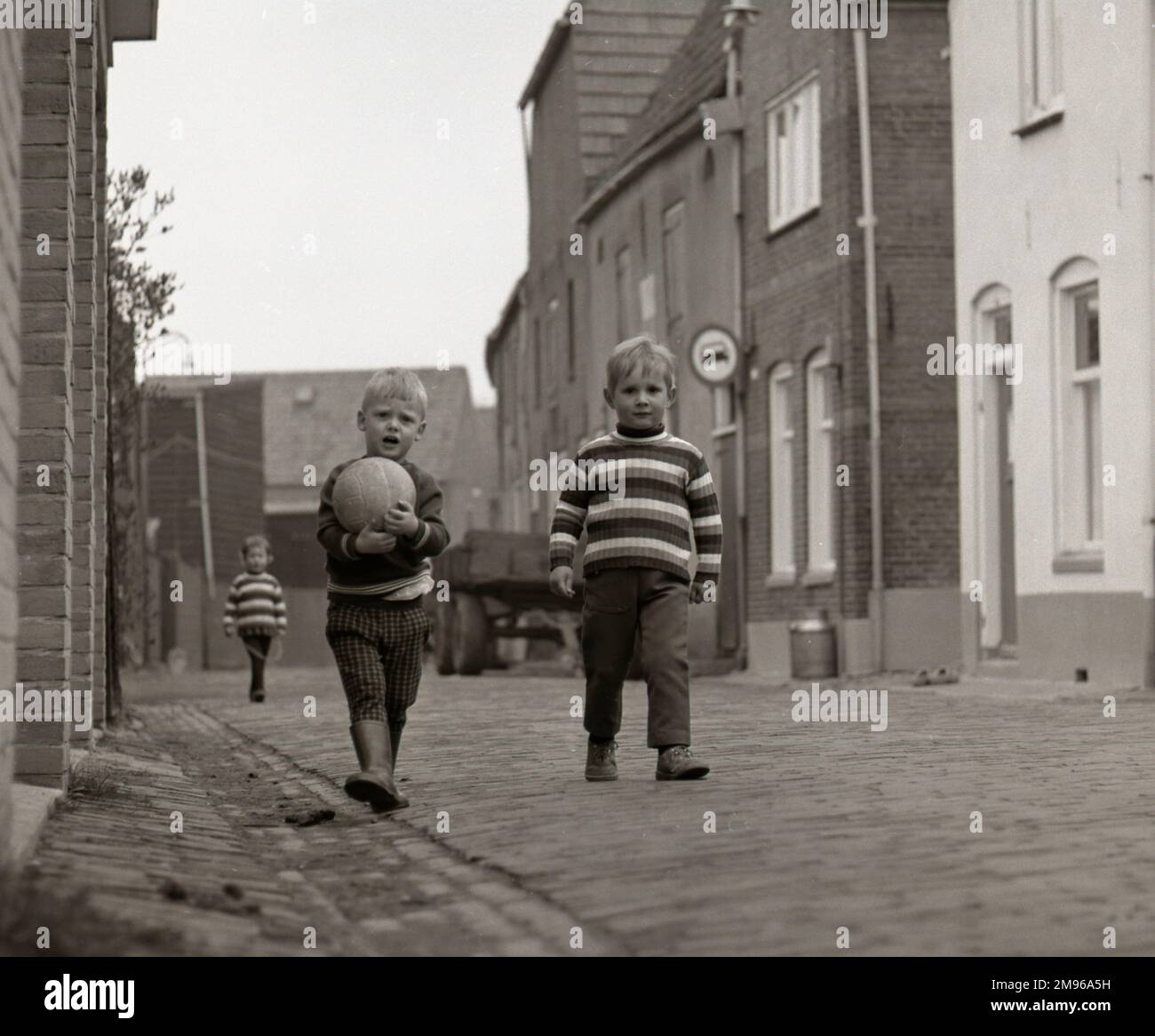 Deux petits garçons dans la rue, l'un dans un chandail strippy et l'autre portant son football. Banque D'Images Deux petits garçons dans la rue, l'un dans un chandail strippy et l'autre portant son football. Banque D'Images