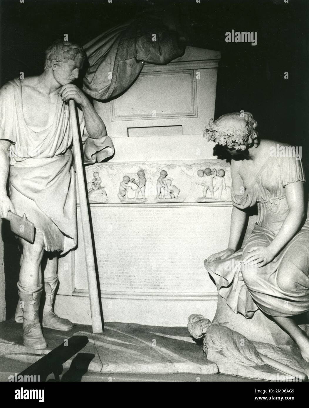 Détail du tombeau de Penrhyn dans l'église de Llandegai (ou Llandygai), près de Bangor, Caernarvonshire (maintenant Gwynedd), au nord du pays de Galles. Le tombeau a été sculpté par Richard Westmacott pour le premier Seigneur et Lady Penrhyn, qui ont été éminentes dans le développement de l'industrie galloise de l'ardoise. Les statues sont d'un quarryman et d'une paysanne, quelque peu idéalisées dans le costume de style grécien, et décrites par Eric Hobsbawm comme 'les premiers prolétaires sculptés'. Il y a un bas relief de chérubins fendant des lattes, et une longue inscription en dessous d'eux. Banque D'Images