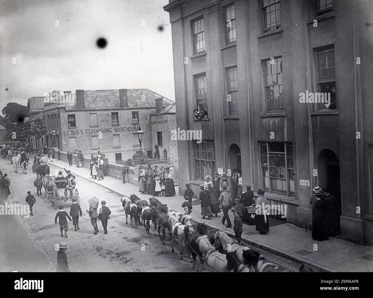 Vue sur la place Salutation pendant la procession du cirque de Sanger, à Haverfordwest, Pembrokeshire, Dyfed, au sud du pays de Galles, avec les garçons suivant dans la chaussée, et les gens regardant des trottoirs et des fenêtres. Lewis's Furnishing Warehouse peut être vu dans l'arrière-plan. Banque D'Images