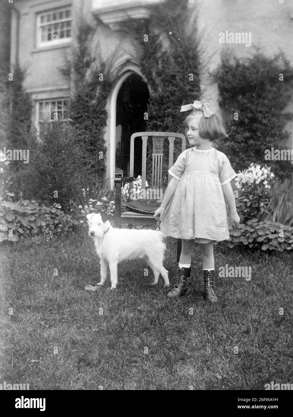 Une petite fille édouardienne dans un jardin avec un petit chien terrier à poil dur. Banque D'Images