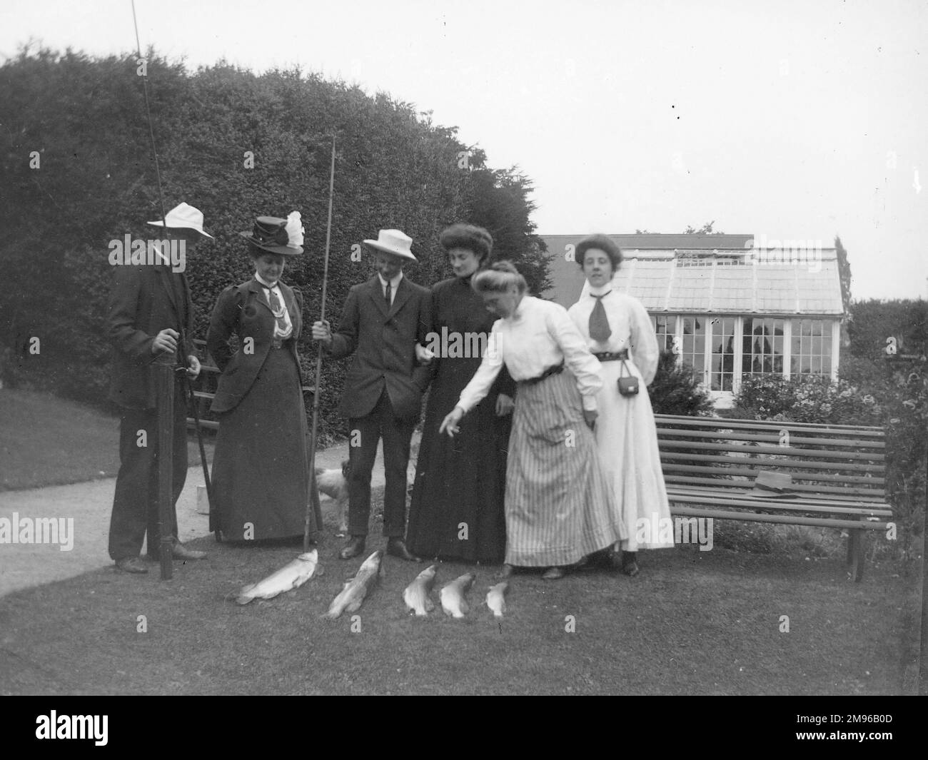 Un groupe d'amis édouardiens inspectant une prise de poisson dans un grand jardin du Pembrokeshire. Les deux hommes, dont l'un est un vicaire, tiennent des cannes à pêche. Les quatre femmes regardent admirablement la gamme de poissons disposés sur l'herbe. Six personnes, cinq poissons - mais beaucoup pour tout le monde! Banque D'Images