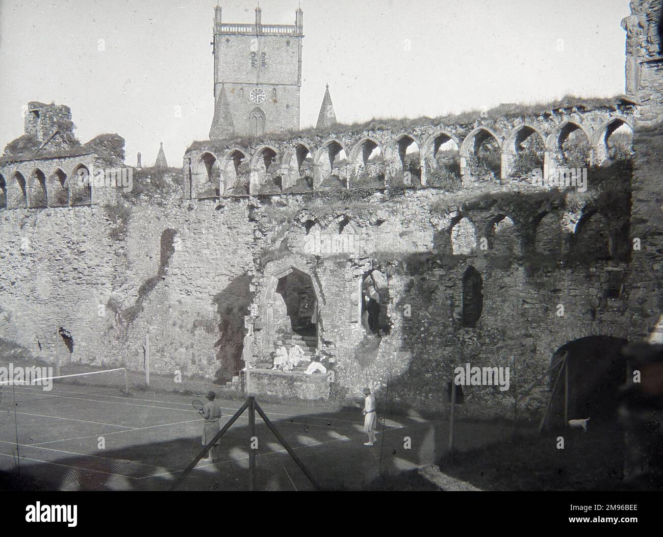 Un court de tennis, avec les gens jouant, à l'intérieur des ruines du Palais de l'évêque médiéval, St David, Pembrokeshire, Dyfed, au sud du pays de Galles. Une rangée d'arches de style gothique où les fenêtres étaient visibles au-dessus, avec la tour de la cathédrale à proximité. Certaines parties du bâtiment datent du 12th siècle, mais la plupart des travaux ont été réalisés au 14th siècle. Banque D'Images
