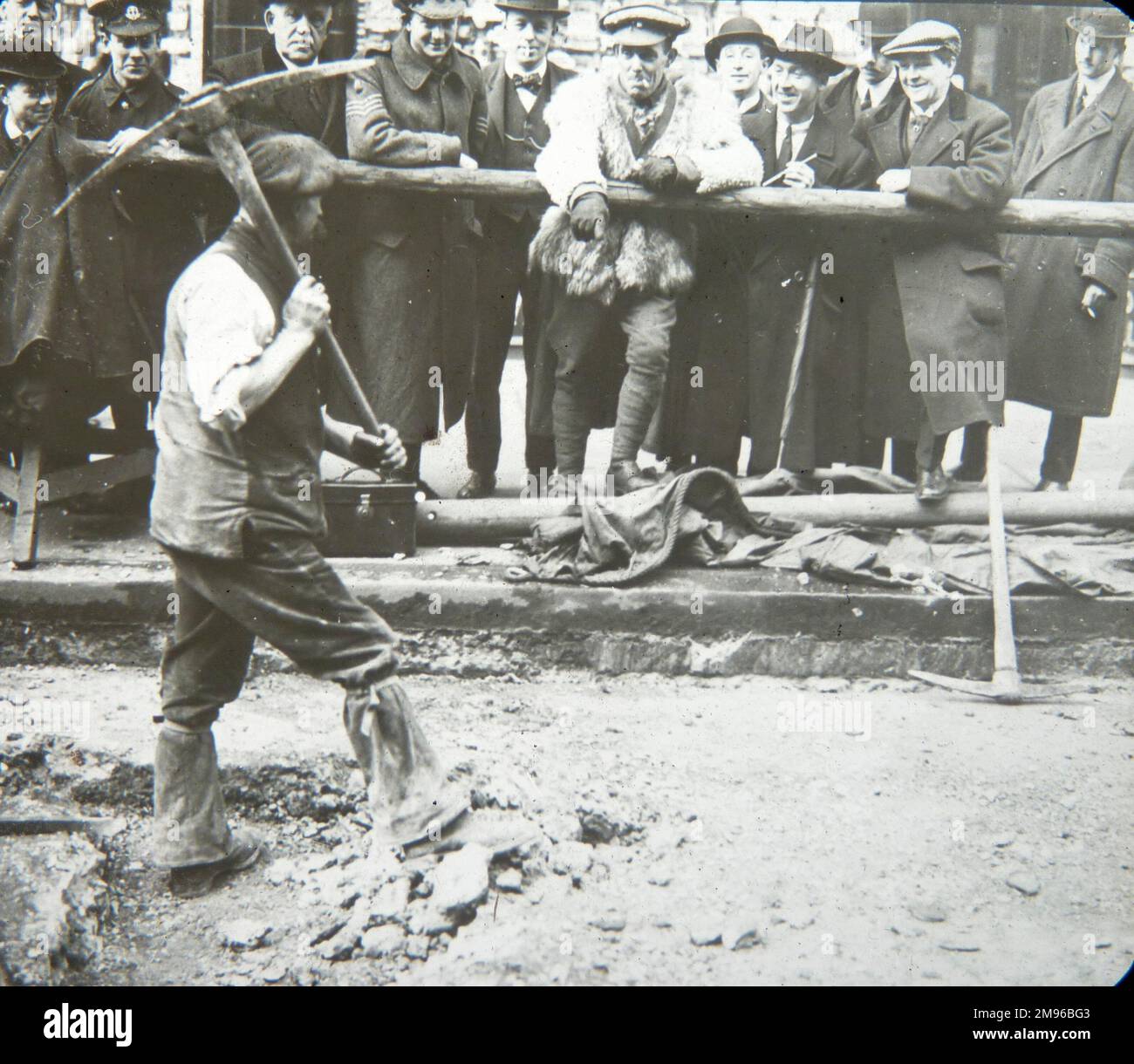 Un groupe de militaires américains, ainsi que quelques civils, observent un homme qui effectue des réparations routières pendant la Seconde Guerre mondiale. Banque D'Images