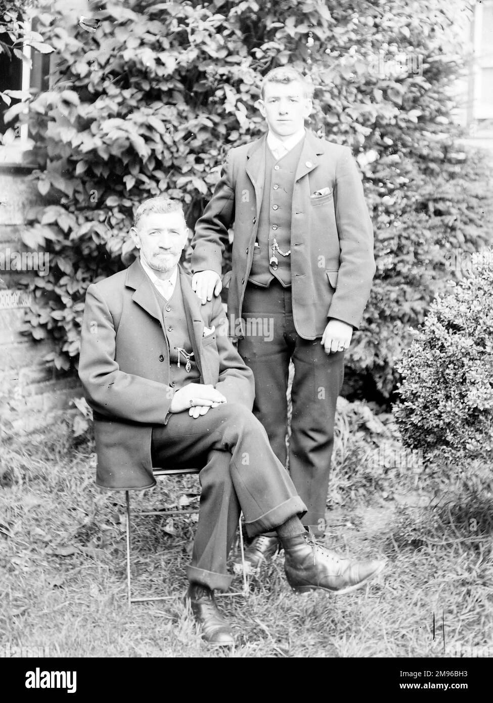 Un père et un fils posent pour leur photo dans un jardin, probablement dans la région du Mid Wales. Ils portent des combinaisons très similaires de trois pièces. Banque D'Images