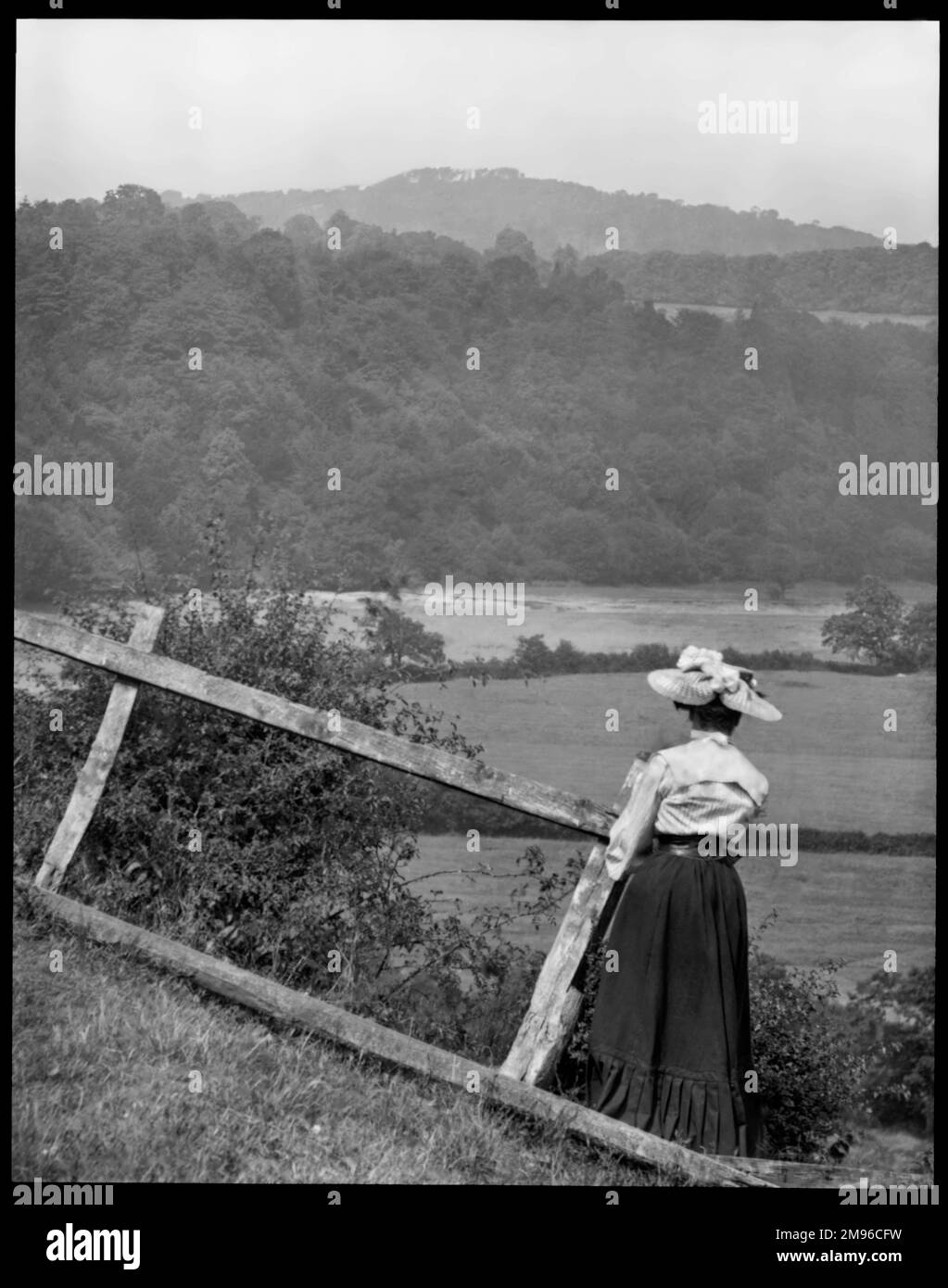 Une femme édouardienne regardant à travers les champs, avec des arbres et des collines au loin. Banque D'Images