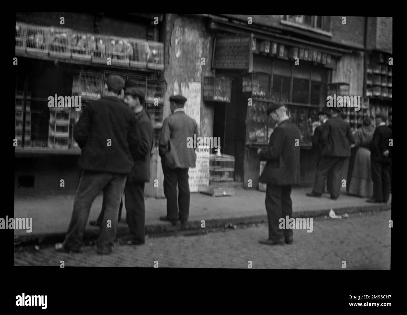 Hommes debout sur la chaussée à l'extérieur d'un marché aux oiseaux dans l'est de Londres. Les oiseaux sont exposés dans de nombreuses cages. C'était peut-être dans la rue Sclater, Shoreditch, près de Bethnal Green, où un marché aux oiseaux a eu lieu chaque dimanche. Banque D'Images