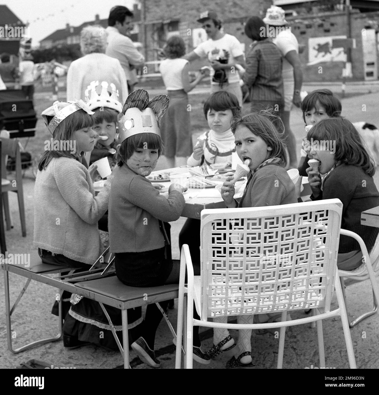 Les enfants en chapeaux de papier s'assoient à une table dans une rue de Crawley, Surrey, et mangent de la glace pour célébrer le Jubilé d'argent de la reine Elizabeth II. Banque D'Images