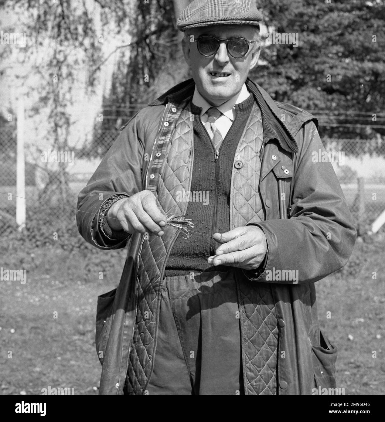 Un pêcheur expérimenté tenant une mouche faite par l'homme dans sa main. Banque D'Images