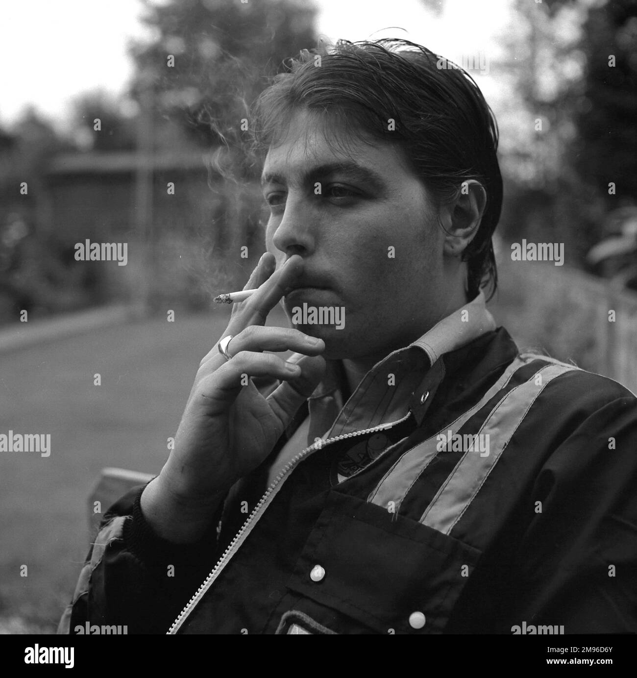 Un jeune homme portant une veste tendance est assis à fumer une cigarette. Banque D'Images