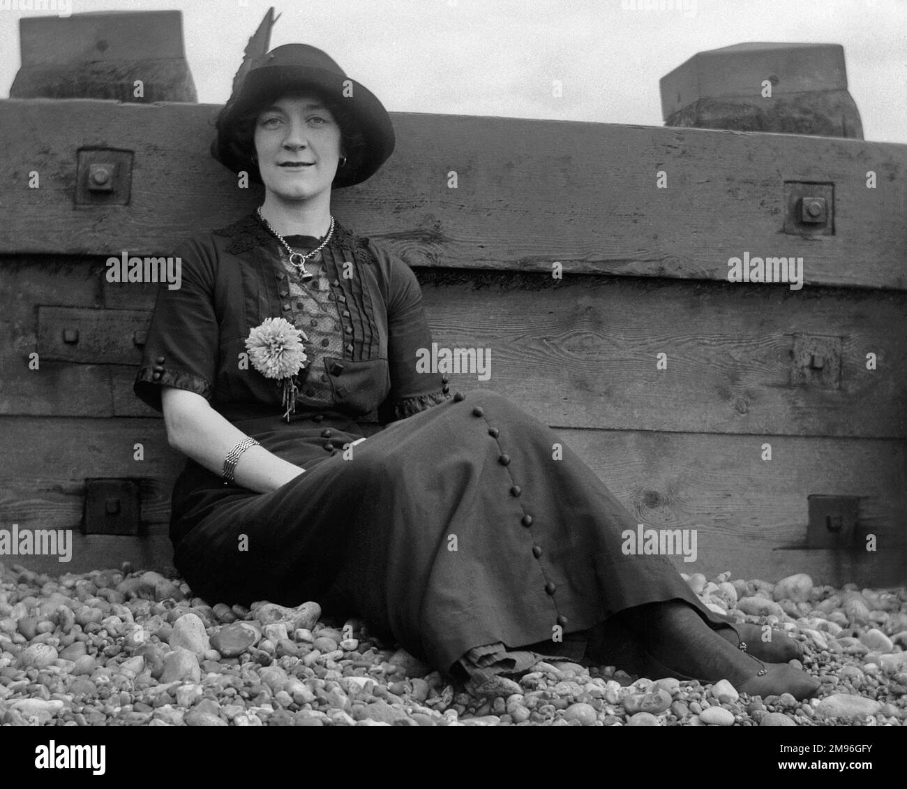 Jeune femme sur une plage de galets, penchée contre un brise-bois. Banque D'Images