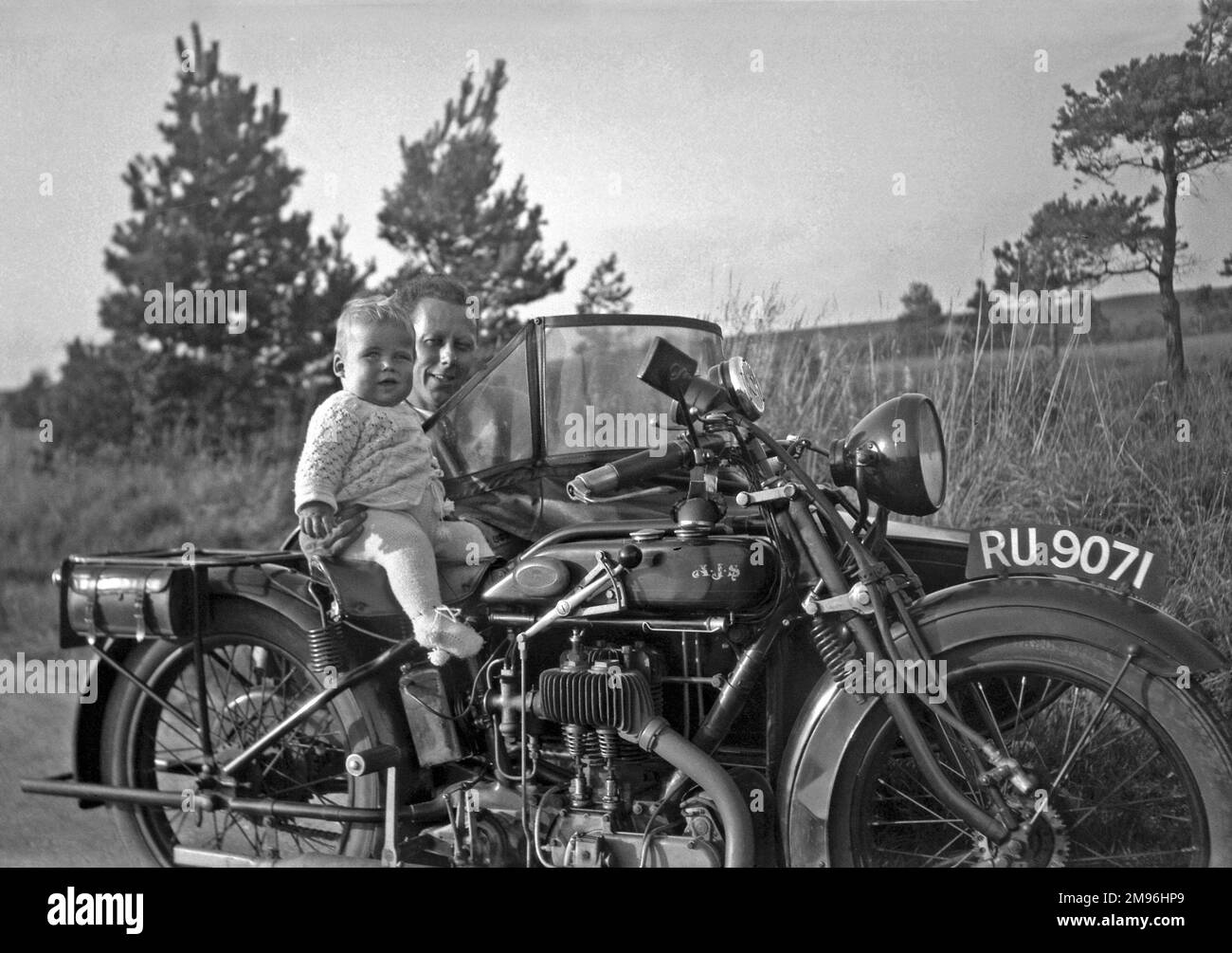 Un homme avec une grande moto et un bébé. Ils semblent avoir échangé des endroits -- le bébé est sur la moto et l'homme est dans le side-car. Banque D'Images
