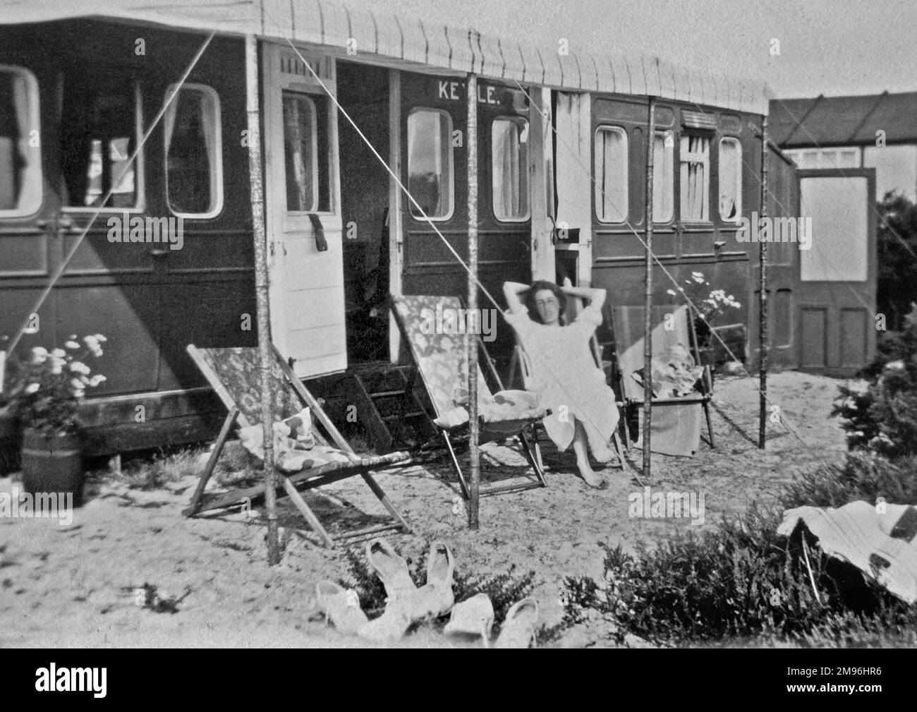 Une femme de vacances assise dans un transat devant une caravane qui semble avoir été adaptée d'un ancien wagon. Banque D'Images