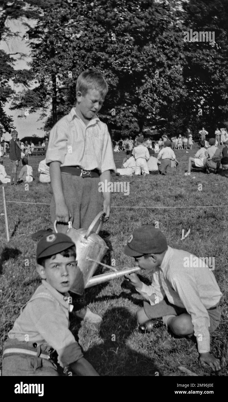 Les écoliers dans un domaine. L'un d'eux essaie de boire de l'entonnoir d'un arrosoir, ou peut-être jouer un morceau dessus. Banque D'Images