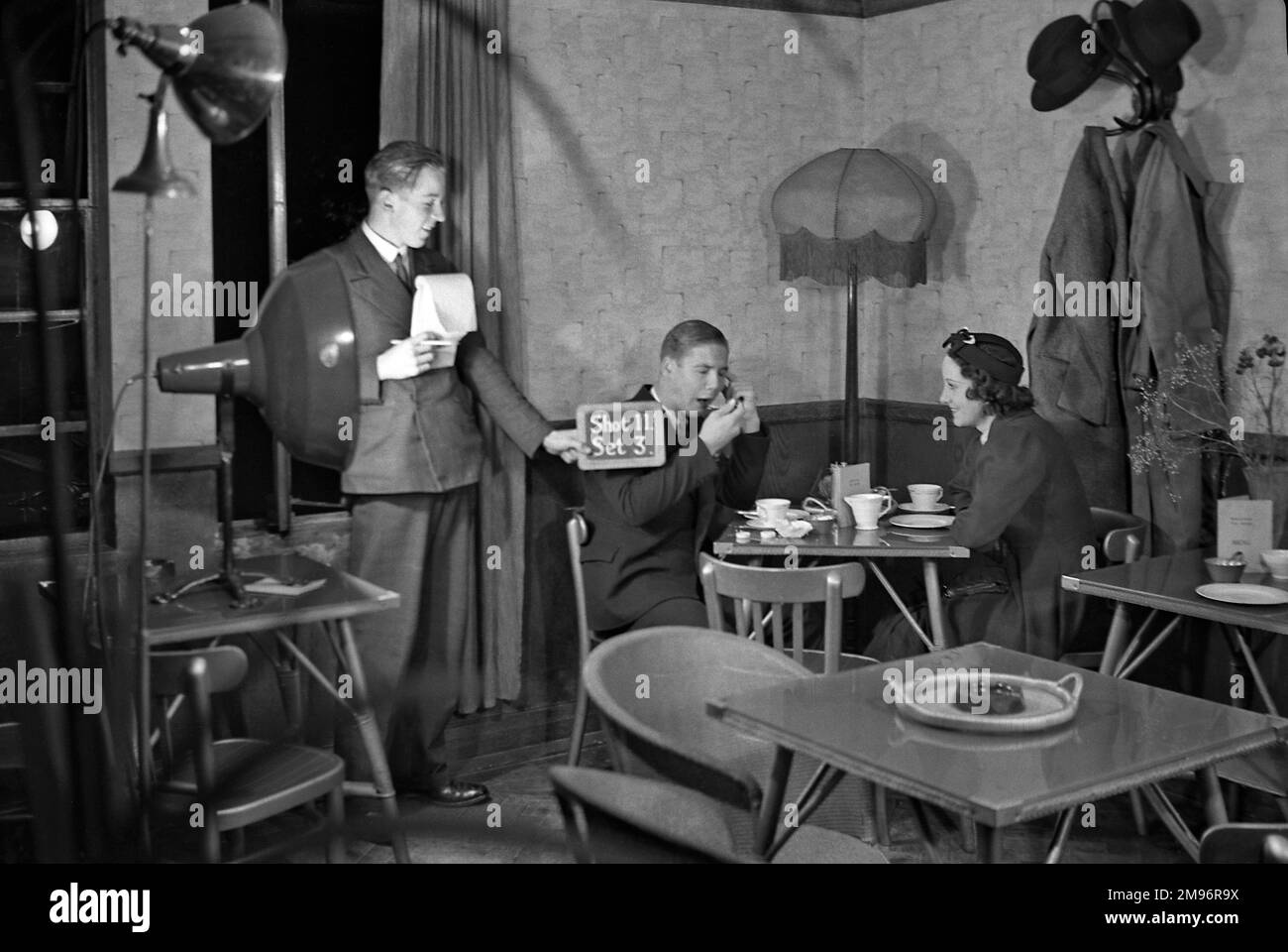 Casting et équipe sur un ensemble de film -- un homme et une femme s'assoient à une table, tandis qu'un autre homme tient une ardoise (photo 11, photo 3). Banque D'Images