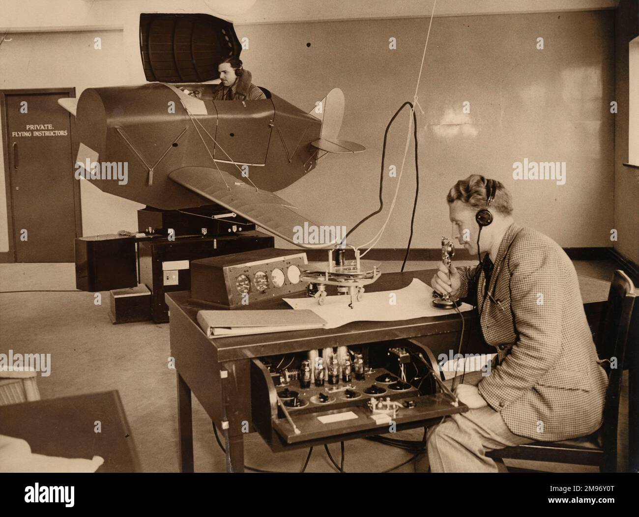 RAF Volunteer Reserve pilote entreprenant des instructions sur un Link Trainer, Gatwick, vers 1940. En reliant la position de l’avion de l’étudiant aux repères sur une carte (effectués par la roue à disque d’un crabe automoteur et orientable), l’instructeur a pu contrôler manuellement la transmission des signaux de balise radio simulés au formateur. Banque D'Images
