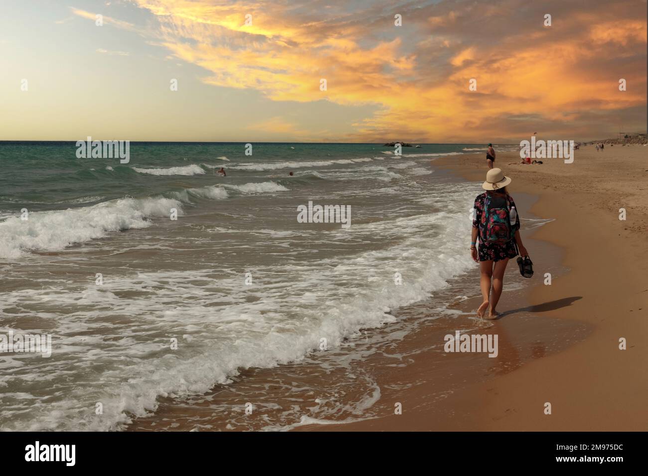 Une femme marchant pieds nus le long de la plage sur le sable. Paysage de vacances. Prise de vue arrière, coucher de soleil, Banque D'Images