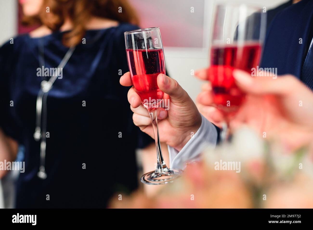coupe de champagne rouge dans la main d'un homme en costume au festival en gros plan. Symbolise le succès et la bonne fortune Banque D'Images
