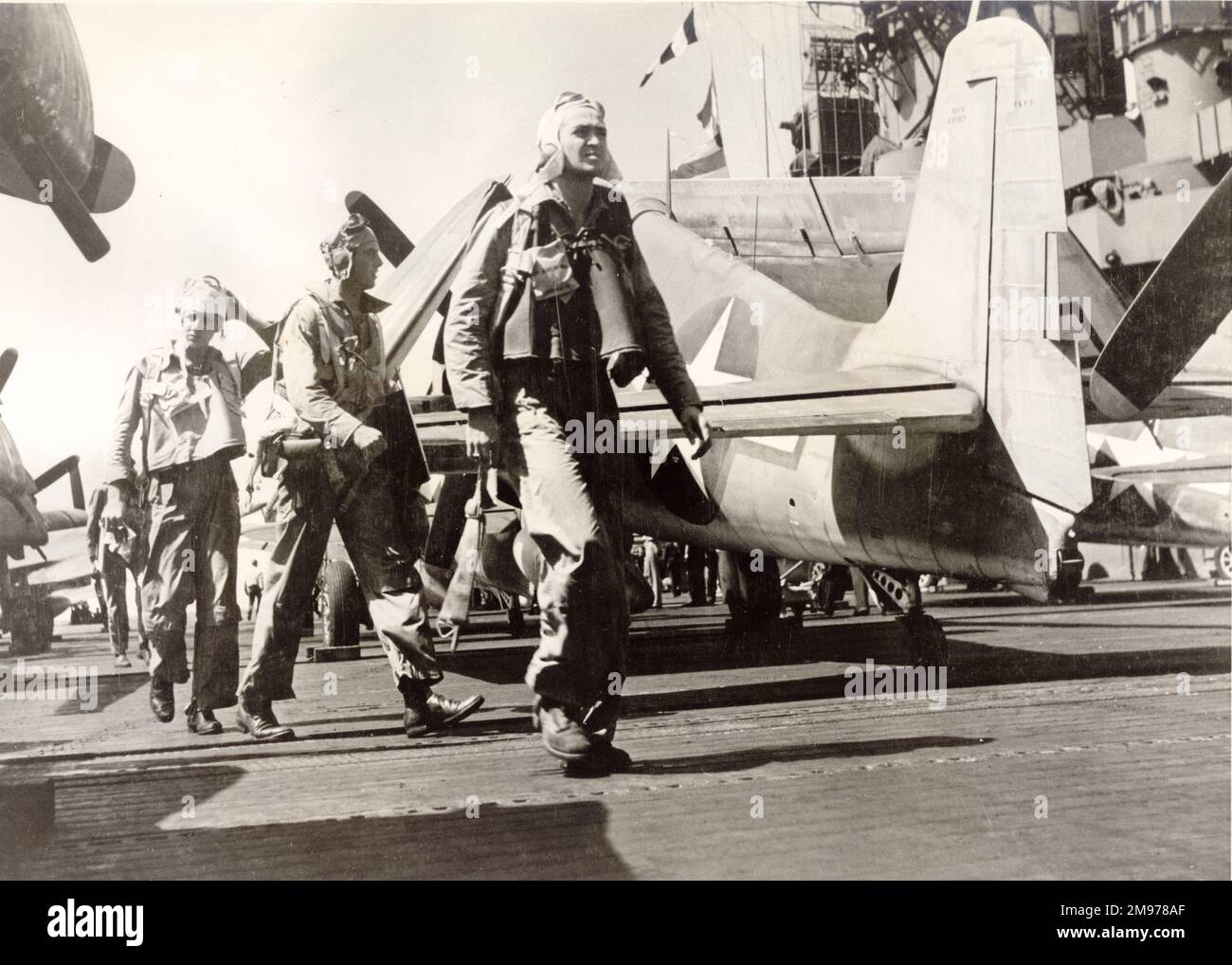 Les pilotes marchent devant un Grumman F6F Hellcat sur un pont porteur. Banque D'Images