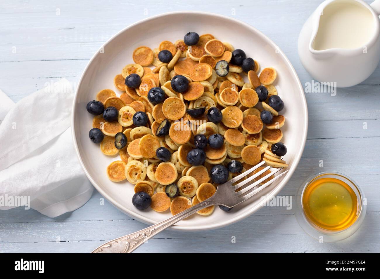 Assiette de mini-crêpes avec crème, miel et baies sur fond bleu clair. Plats tendance. Petit déjeuner maison. Vue sur le dessus Banque D'Images
