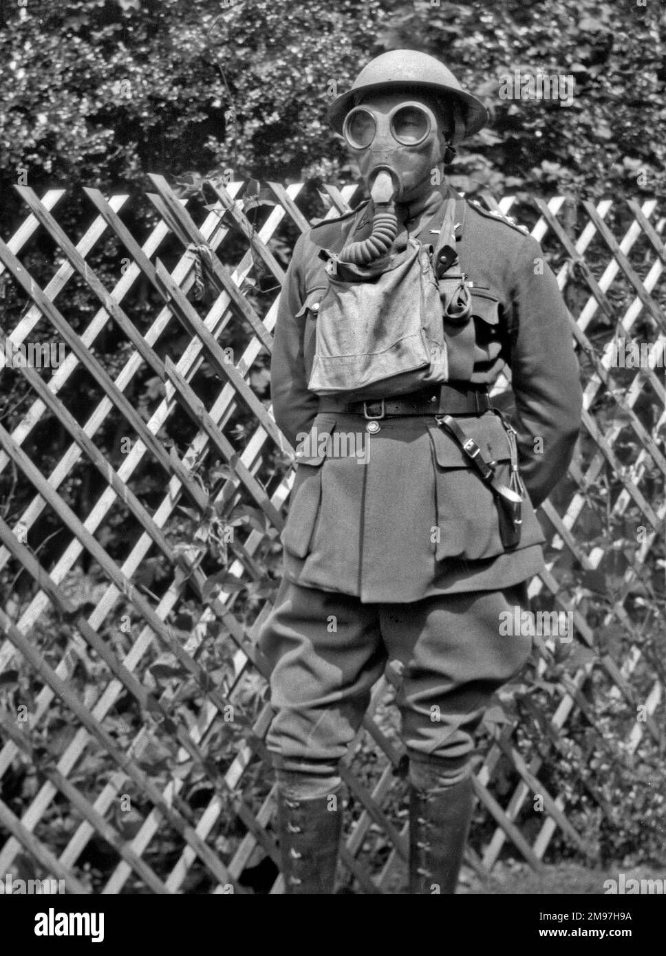 Homme en uniforme, casque en étain et masque à gaz, posé dans un jardin, probablement pendant la Seconde Guerre mondiale. Banque D'Images