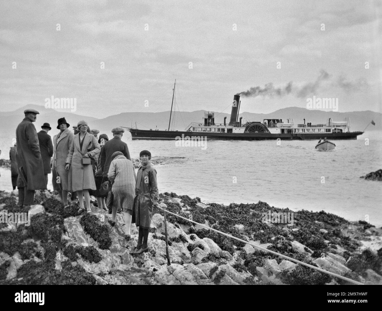 Un groupe de personnes debout sur une côte rocheuse avec un bateau à vapeur sur la mer au loin. Banque D'Images