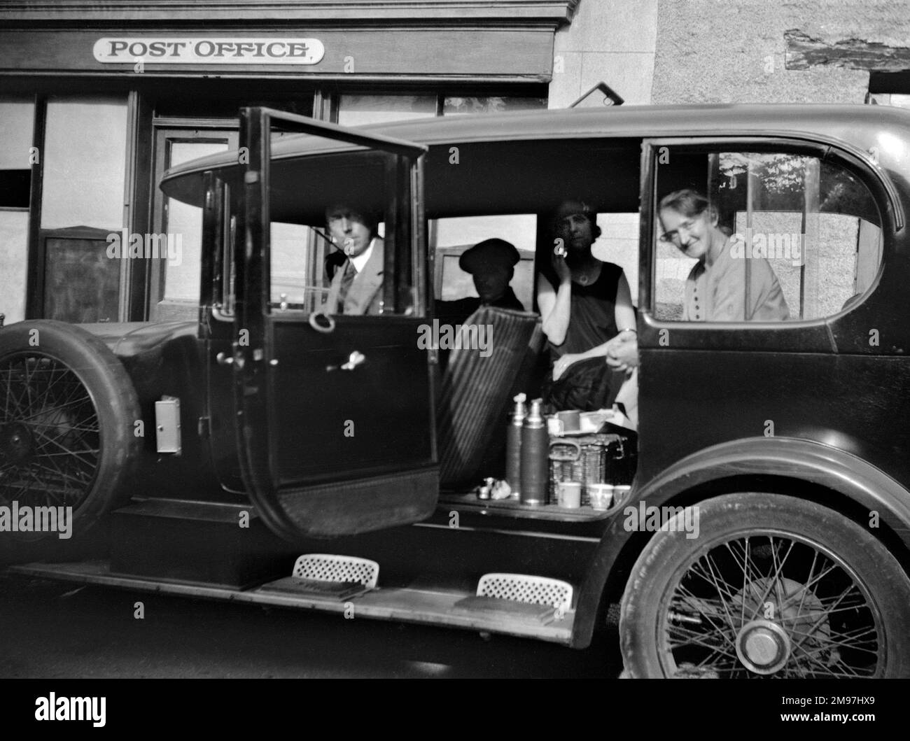 Quatre personnes assises à l'intérieur d'une voiture à l'extérieur d'un bureau de poste avec leurs pique-niques. Banque D'Images
