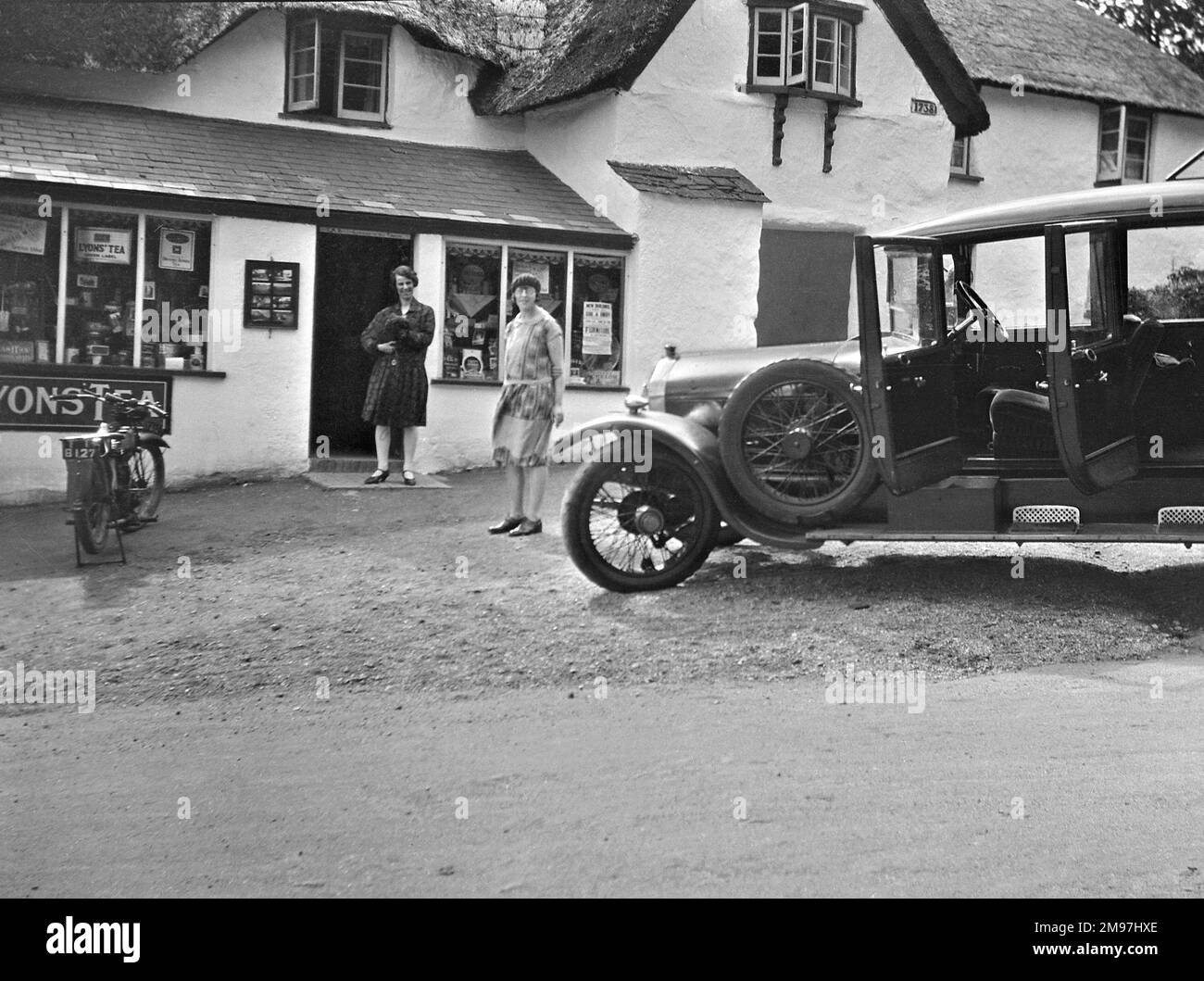 Deux femmes à l'extérieur d'un magasin de village avec leur voiture debout attendant avec les portes ouvertes. Banque D'Images