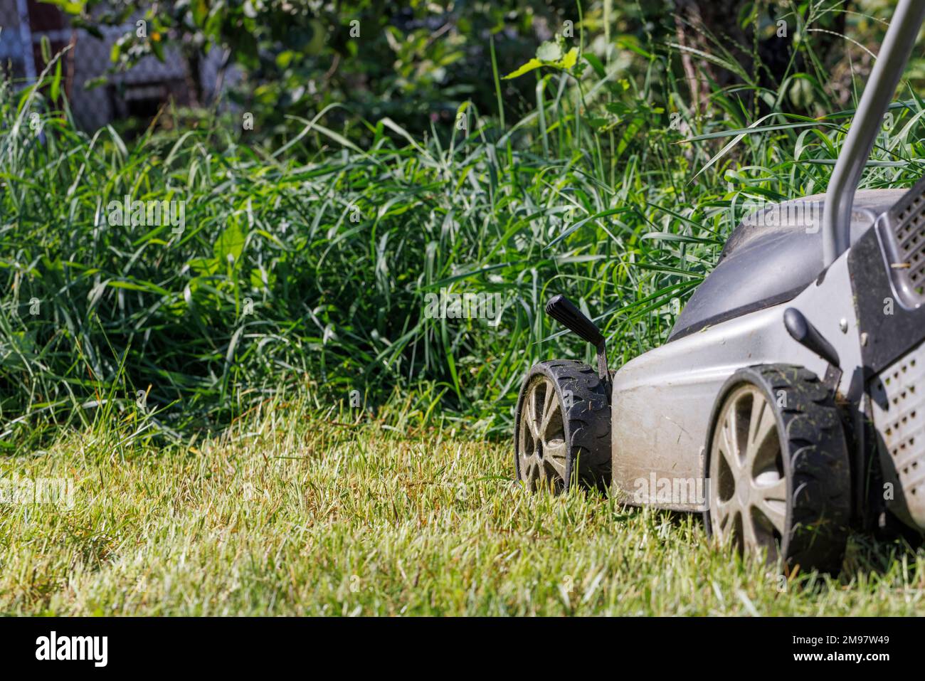Les roues d'une tondeuse à gazon électrique sur fond d'herbe verte dense et brouillée. Banque D'Images
